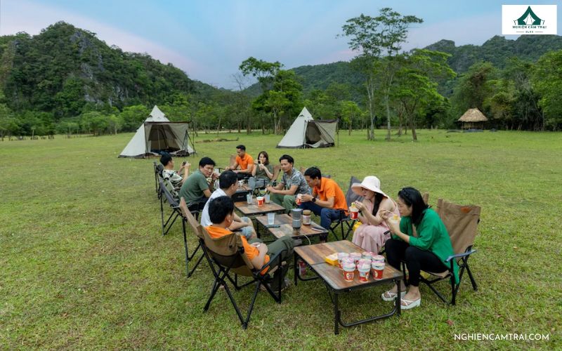 Cả nhóm quây quần thưởng thức bữa tối giữa thung lũng xanh mát, phía sau là lều trại và núi rừng hùng vĩ – khoảnh khắc đáng nhớ tại Thung lũng Tình Yêu Quảng Bình.