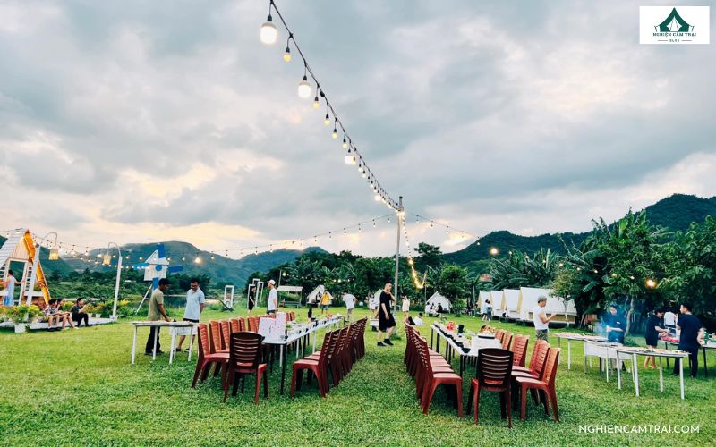 Không gian tiệc nướng BBQ ấm cúng tại Làng Mê Đà Nẵng, nơi bàn tiệc được bày biện giữa thảm cỏ xanh và ánh đèn lung linh giữa núi rừng.