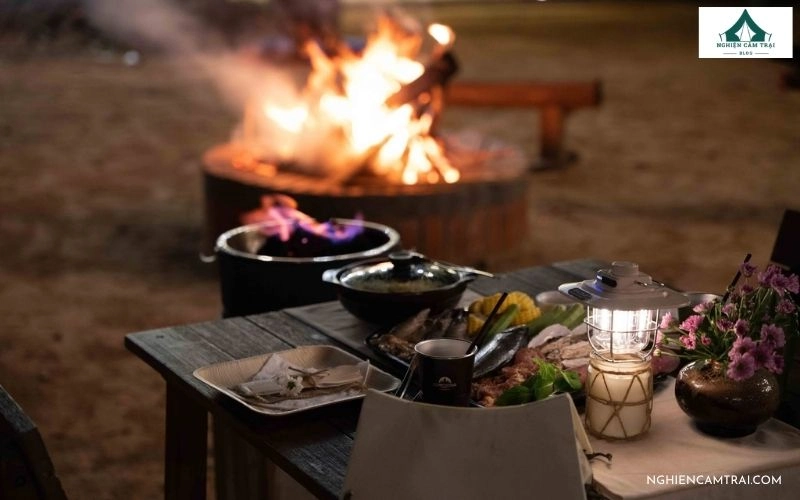 Bàn tiệc BBQ ngoài trời hấp dẫn bên ánh đèn vàng và đống lửa trại ấm áp tại Zenna Pool Camp